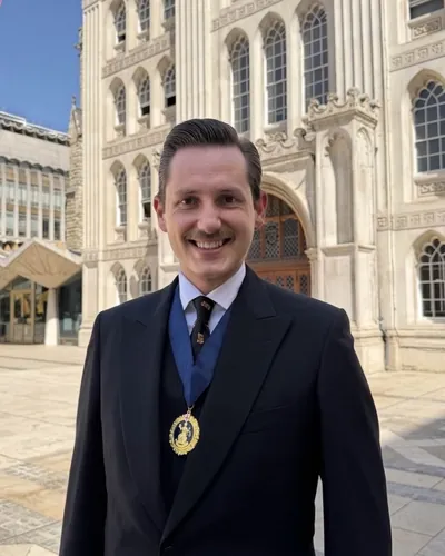 Liam Randall outside Guildhall in a dark suit and tie, smiling, wearing the Ale-Conner badge of office on a blue ribbon
